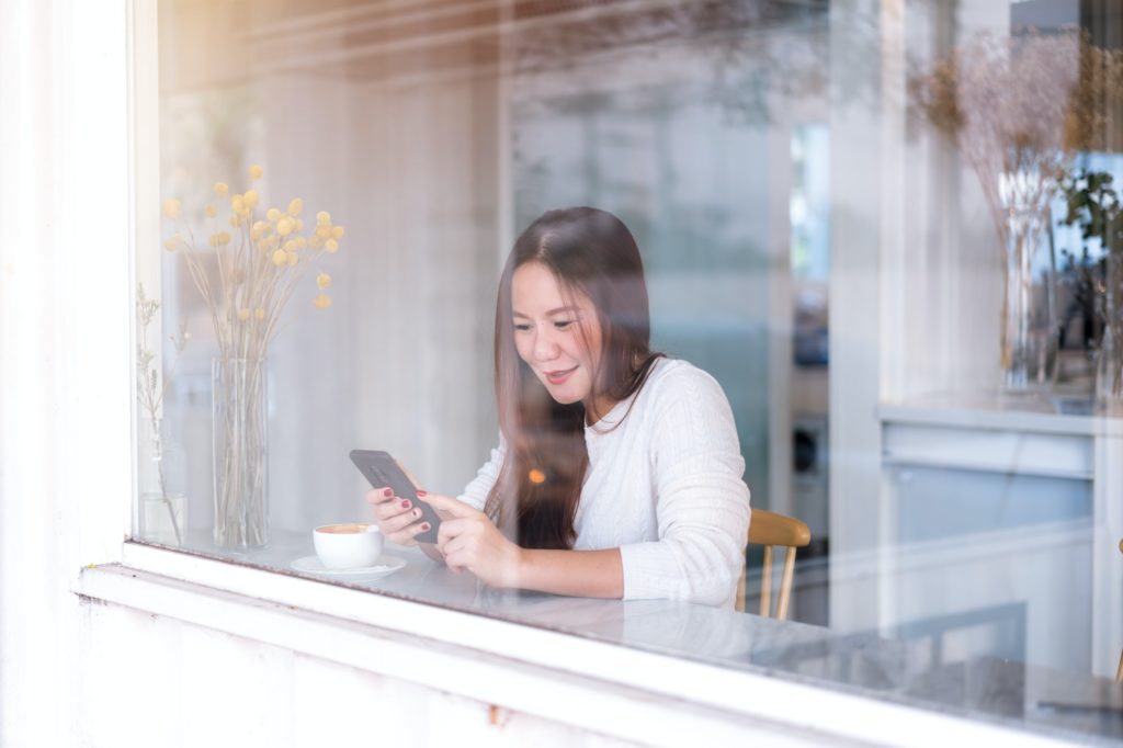 Young entrepreneur business woman relax using phone, shot through a glass window in coffee shop.